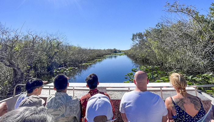 Tourists on an airboat in Everglades National Park, Miami, surrounded by water and vegetation.