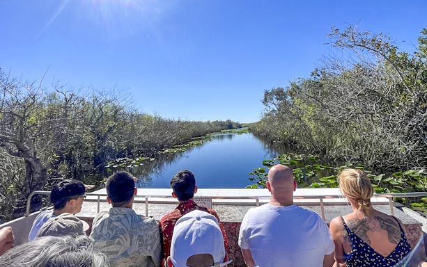 Tourists on an airboat in Everglades National Park, Miami, surrounded by water and vegetation.