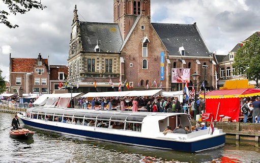 Canal cruise boat passing Alkmaar's historic buildings and market.
