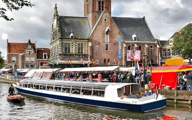 Canal cruise boat passing Alkmaar's historic buildings and market.