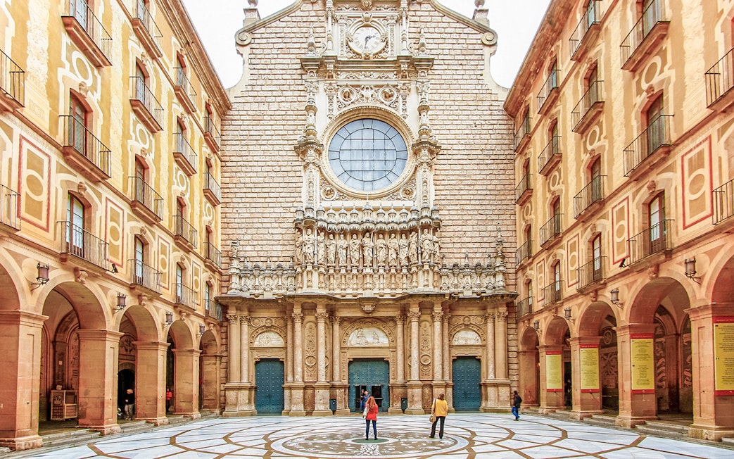 Montserrat Monastery courtyard with detailed facade and visitors exploring.