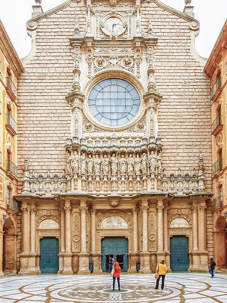 Montserrat Monastery courtyard with detailed facade and visitors exploring.