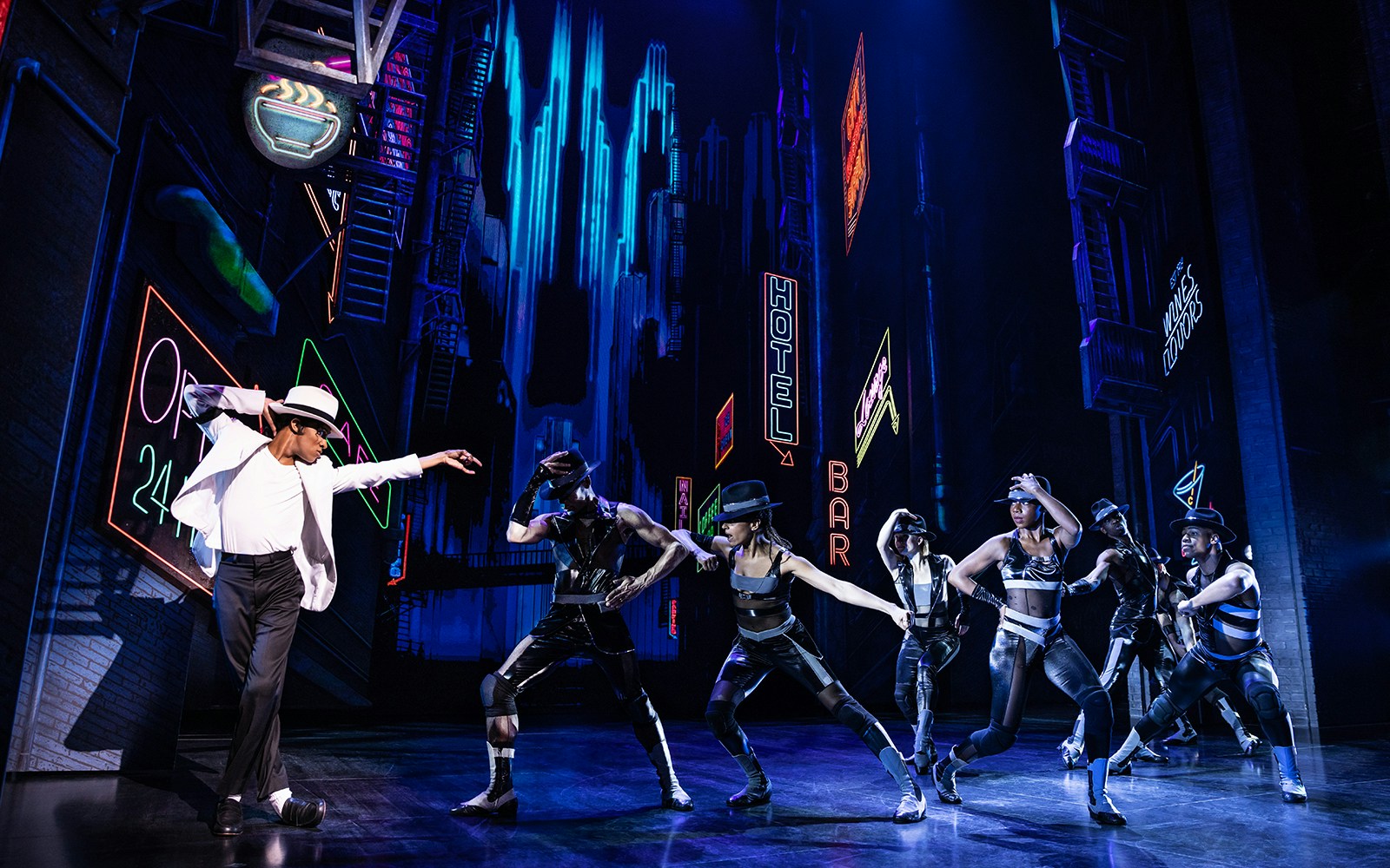Performers dancing on stage at MJ Live tribute concert with neon city backdrop.