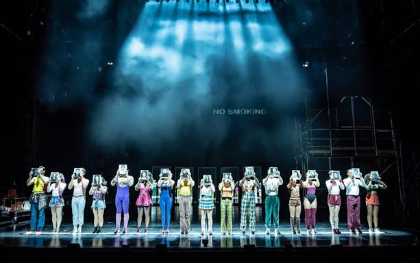 Performers on stage holding headshots in a scene from A Chorus Line musical.