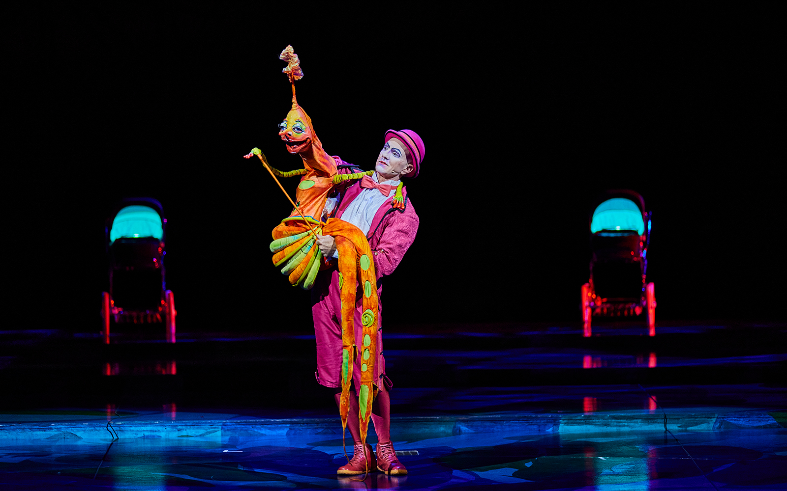 Performer in colorful costume with puppet at Mystère show.
