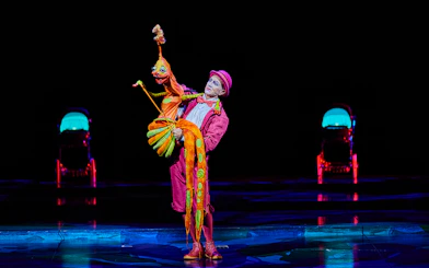 Performer in colorful costume with puppet at Mystère show.
