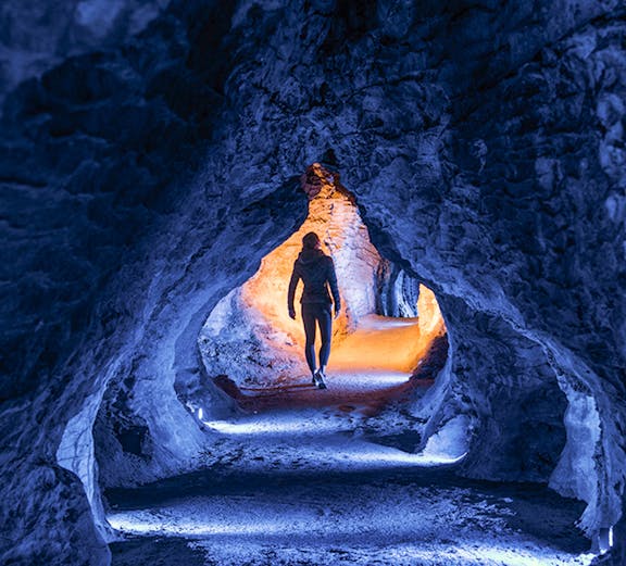 Person walking through illuminated Ruakuri Cave passage, New Zealand.