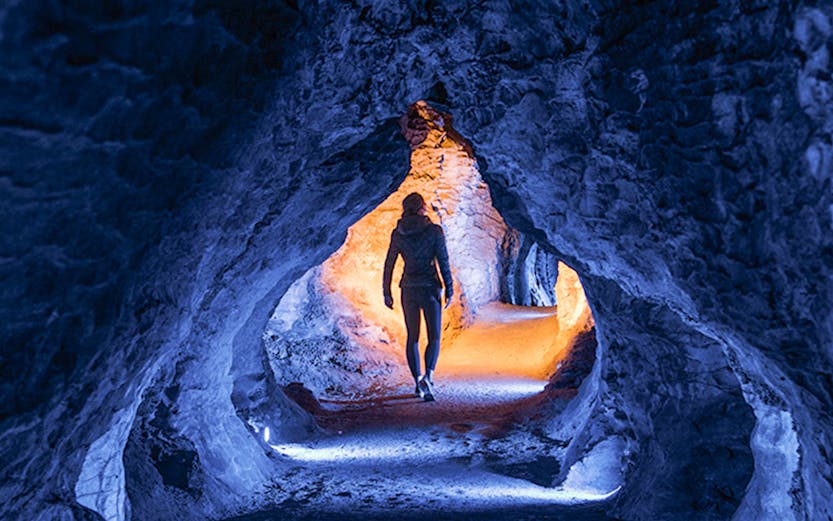 Person walking through illuminated Ruakuri Cave passage, New Zealand.