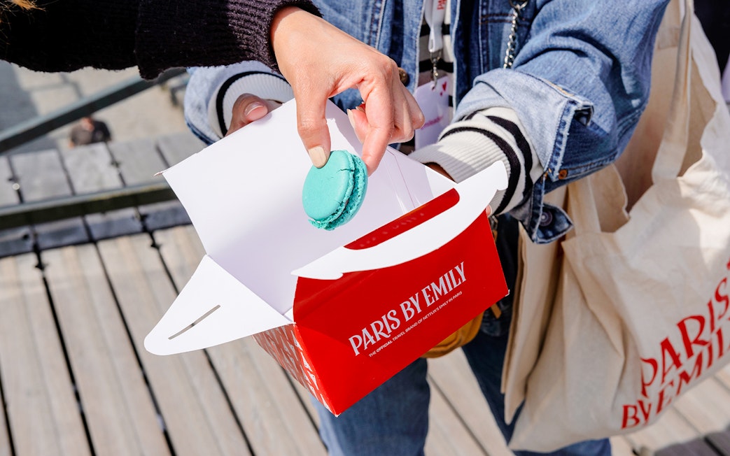 Person taking a macaron from a Paris by Emily box during food tour.