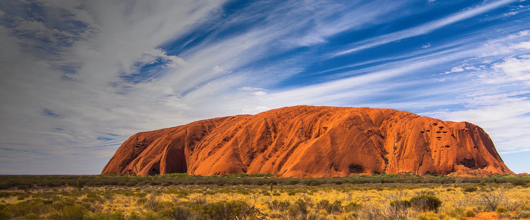 Uluru rock formation under a blue sky in Australia.