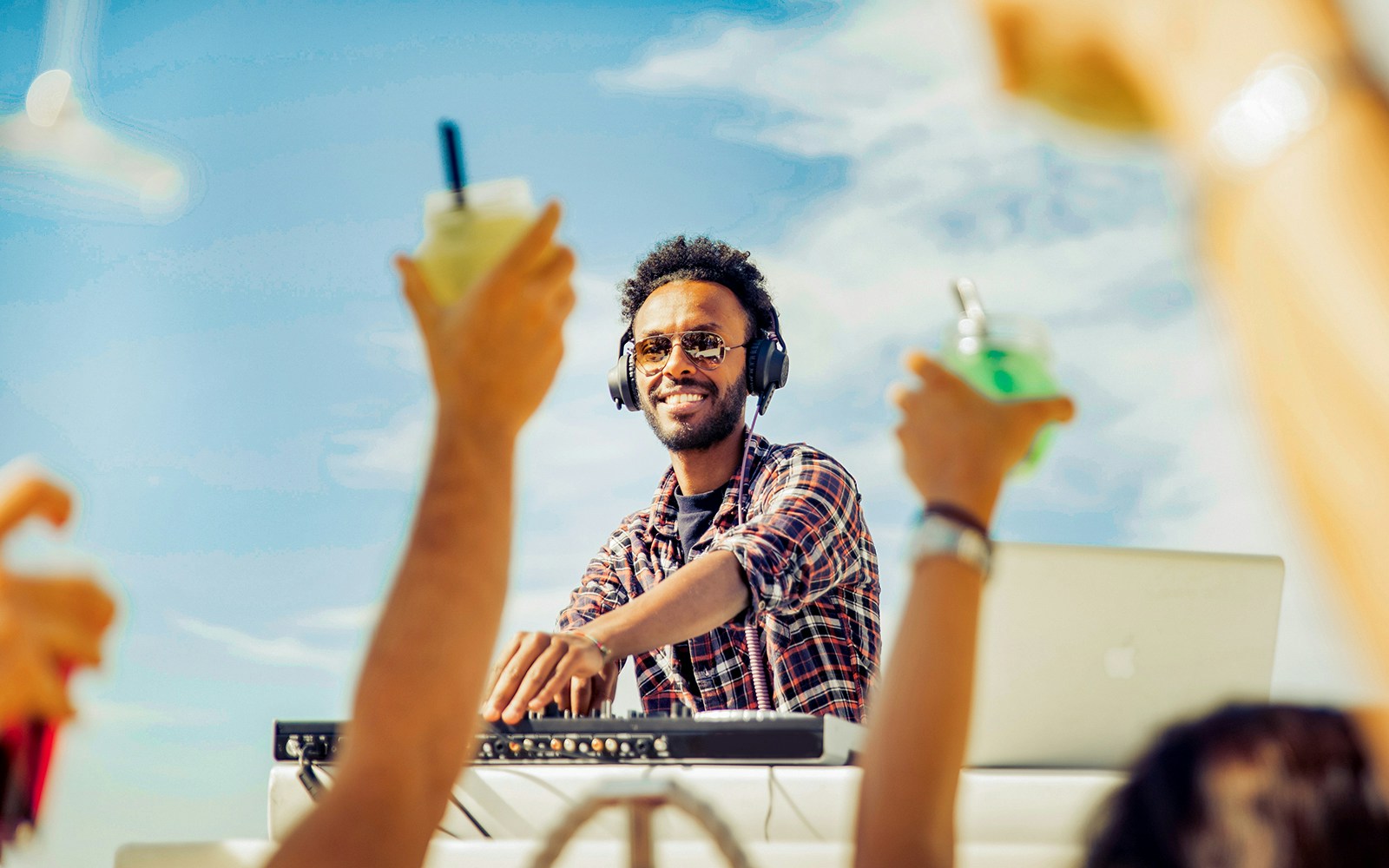 DJ performing on a cruise deck with people raising drinks.
