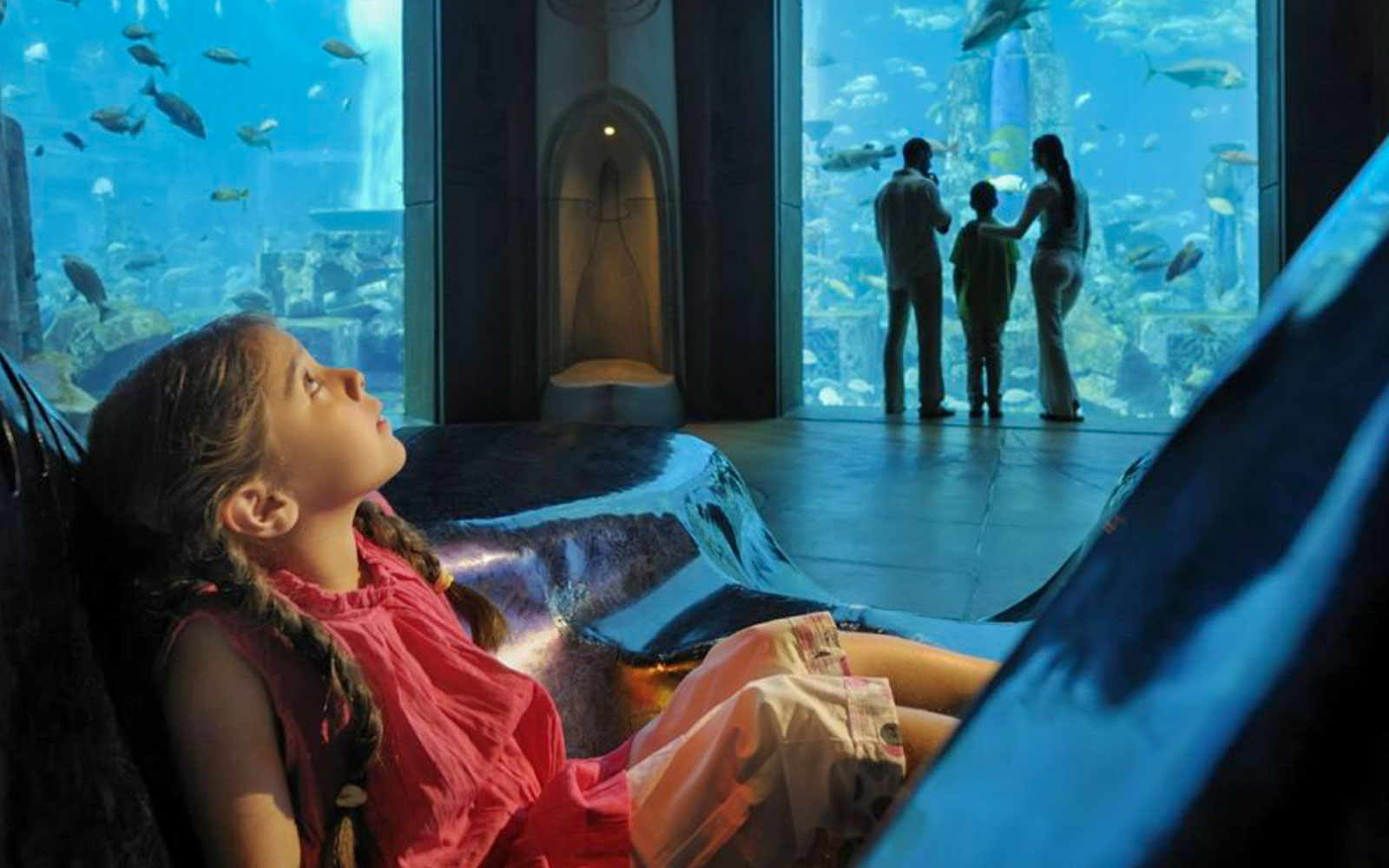 Child observing fish at Aquaventure's Lost World Aquarium, family in background.
