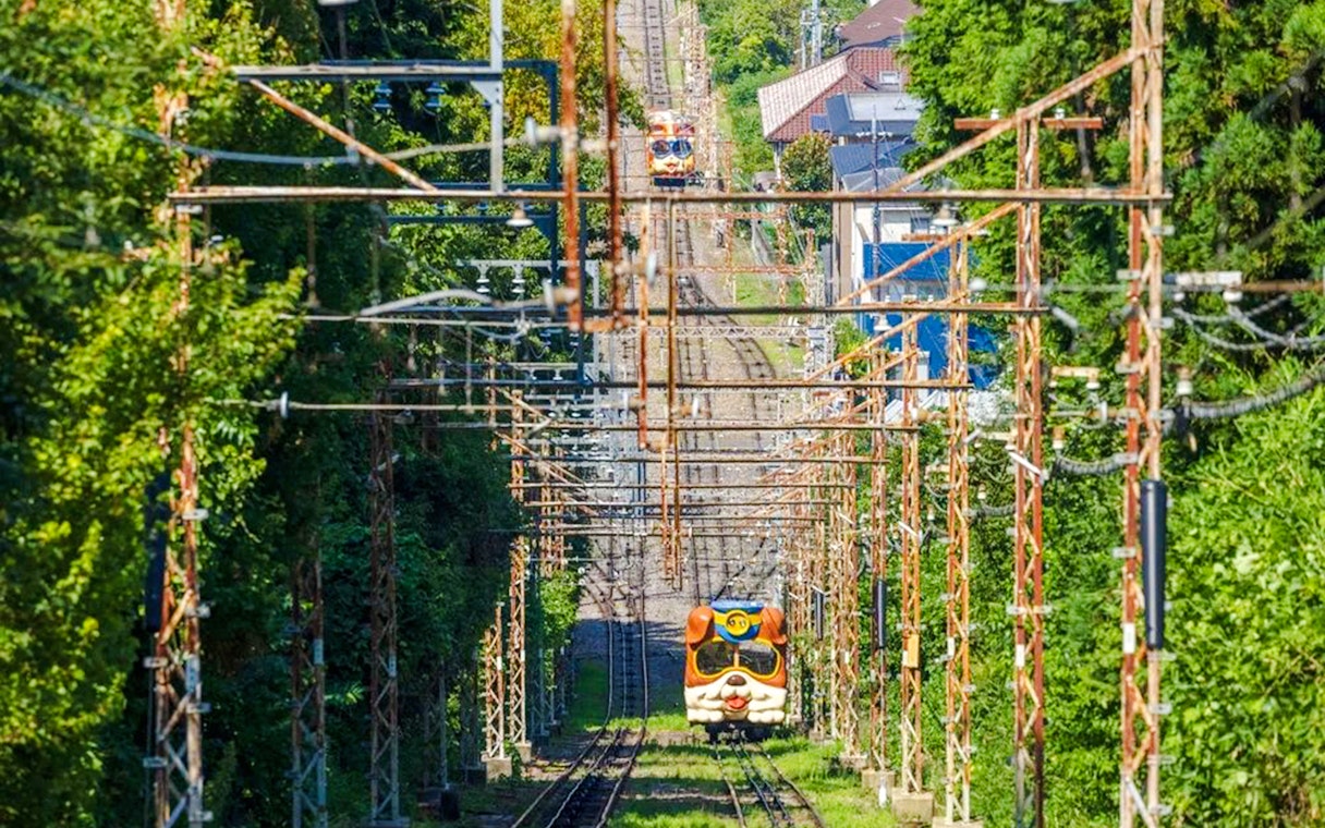 Kintetsu Rail train with animal-themed design traveling through lush greenery.