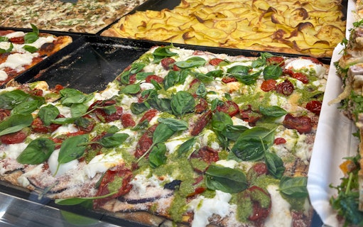 Roman-style pizza with fresh basil, tomatoes, and mozzarella on display.