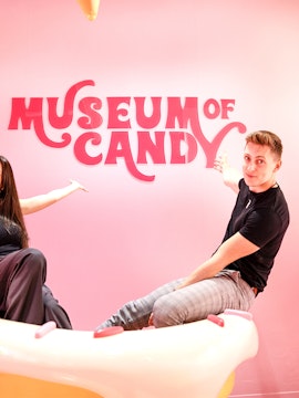 Visitors pointing at Museum of Candy sign on a pink wall.