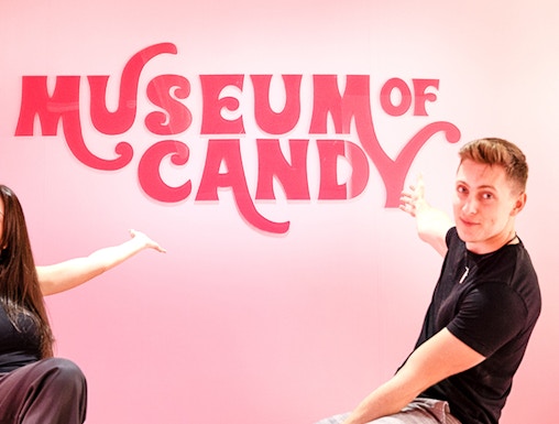 Visitors pointing at Museum of Candy sign on a pink wall.