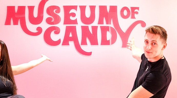 Visitors pointing at Museum of Candy sign on a pink wall.