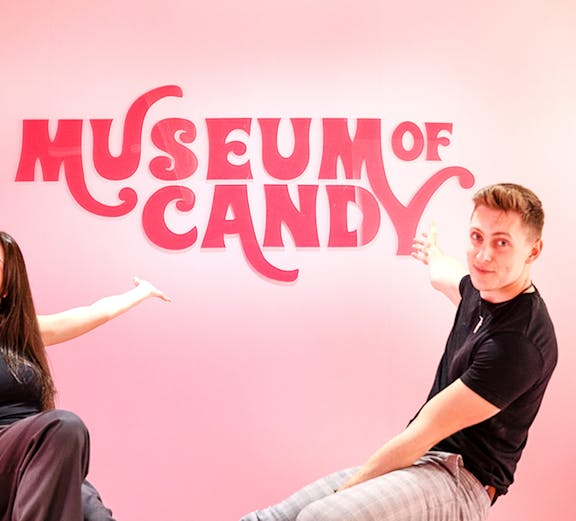 Visitors pointing at Museum of Candy sign on a pink wall.