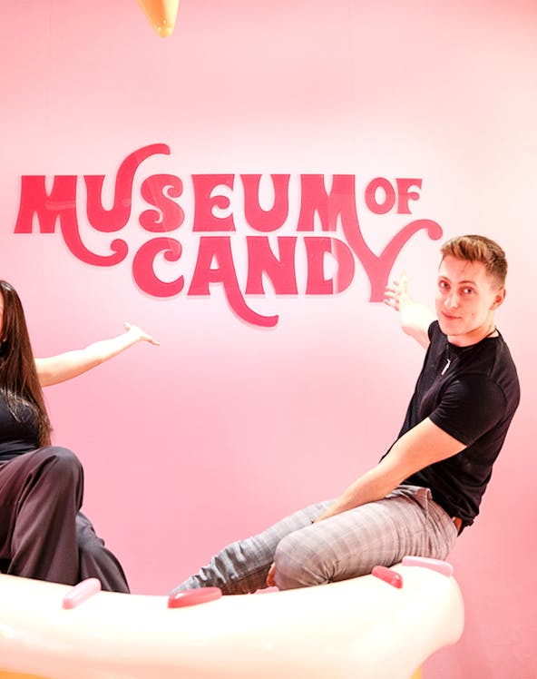 Visitors pointing at Museum of Candy sign on a pink wall.