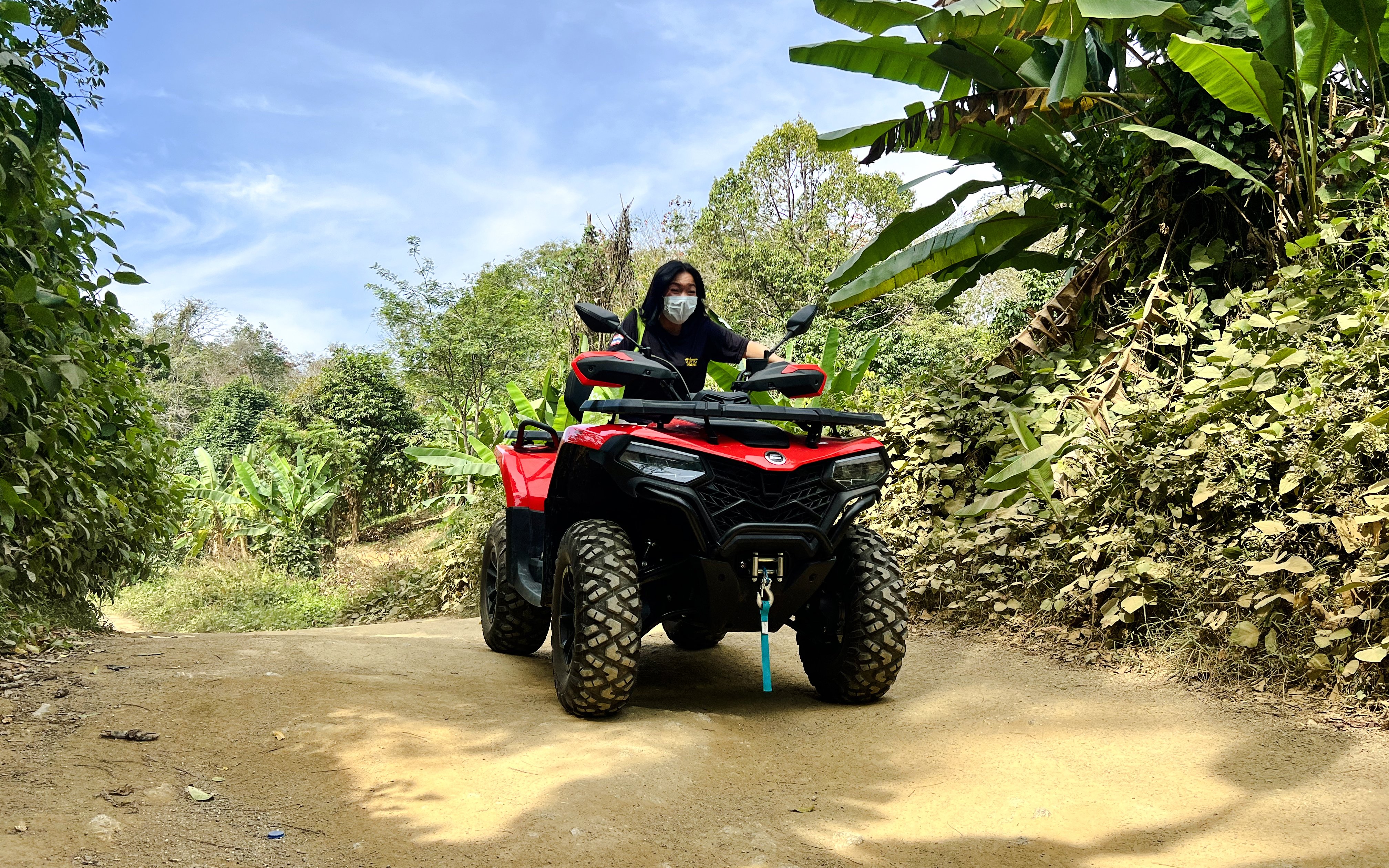 Girl riding red ATV on a dirt path through lush greenery.