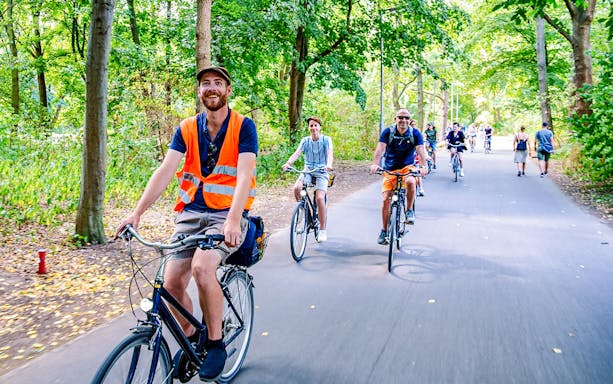 Cyclists on a guided bike tour through a tree-lined path in Berlin.