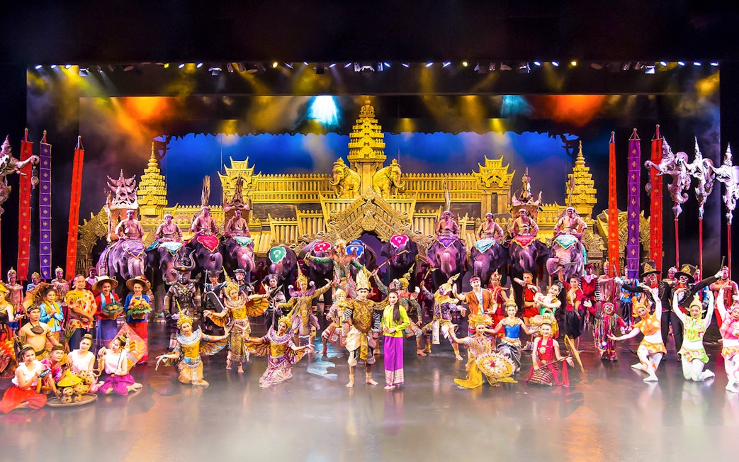 Performers in traditional costumes on stage at Phuket Fantasea with elephants and ornate backdrop.