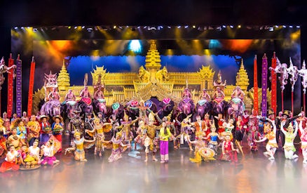 Performers in traditional costumes on stage at Phuket Fantasea with elephants and ornate backdrop.
