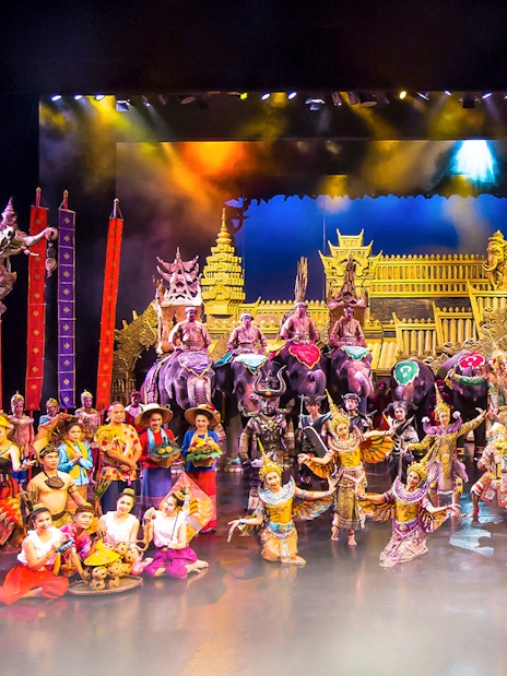 Performers in traditional costumes on stage at Phuket Fantasea with elephants and ornate backdrop.