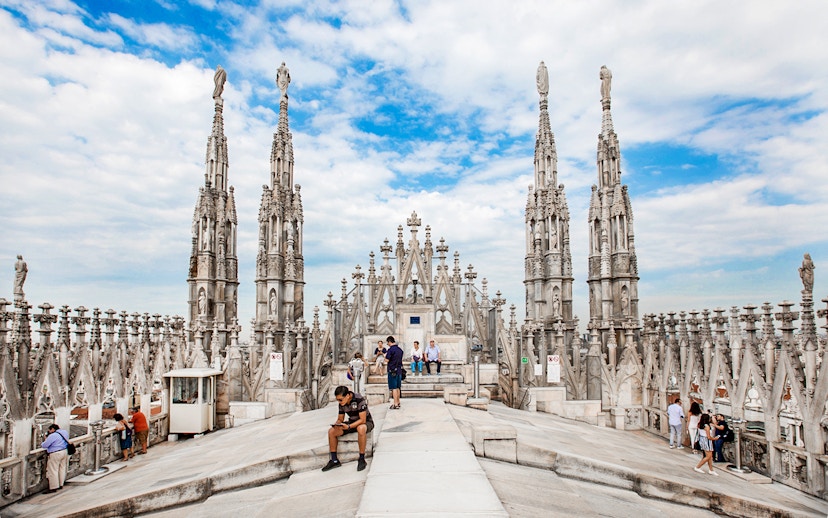 Tourists exploring rooftop of Duomo Cathedral, Milan with spires in view.