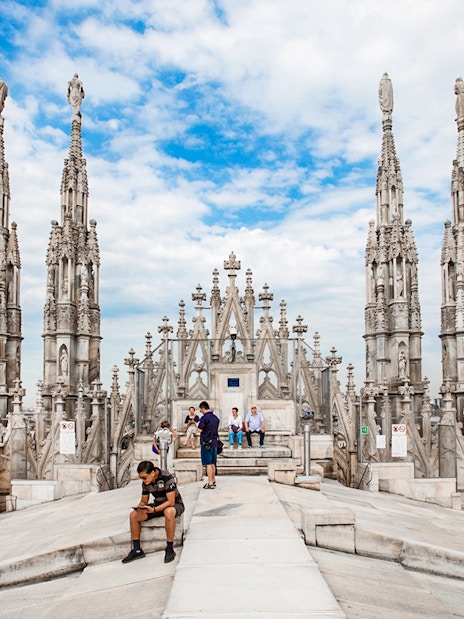 Tourists exploring rooftop of Duomo Cathedral, Milan with spires in view.