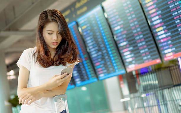 Traveler checking phone at Central Japan International Airport with flight information board.