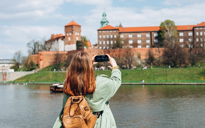 Tourist photographing Wawel Castle from across the Vistula River in Krakow.