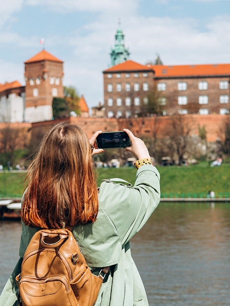 Tourist photographing Wawel Castle from across the Vistula River in Krakow.