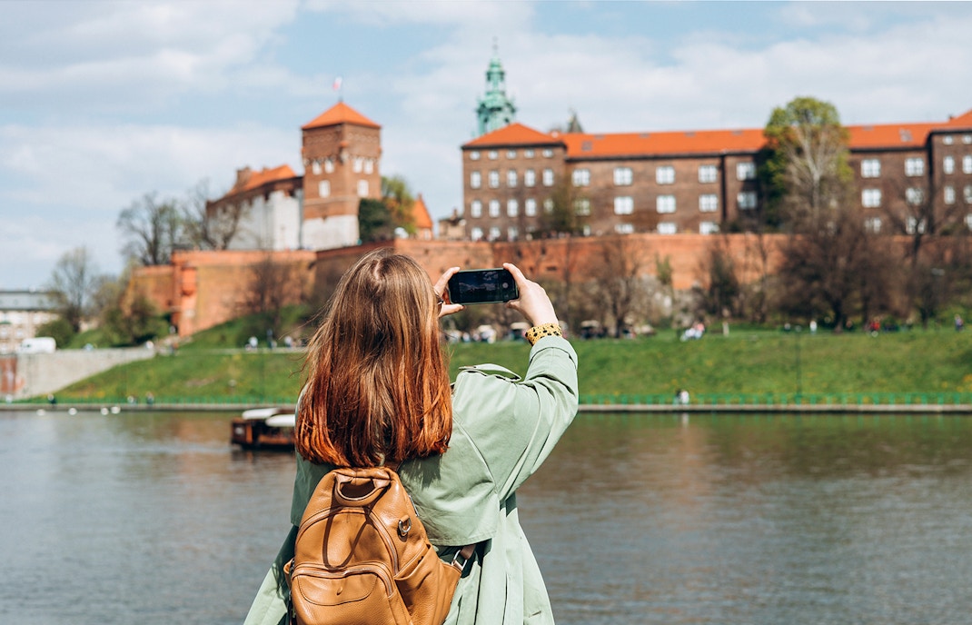 Tourist photographing Wawel Castle from across the Vistula River in Krakow.