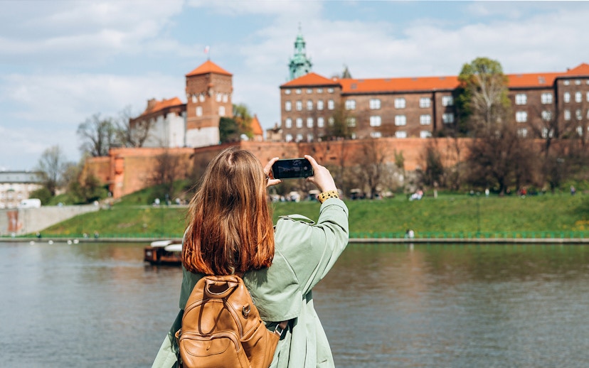 Tourist photographing Wawel Castle from across the Vistula River in Krakow.