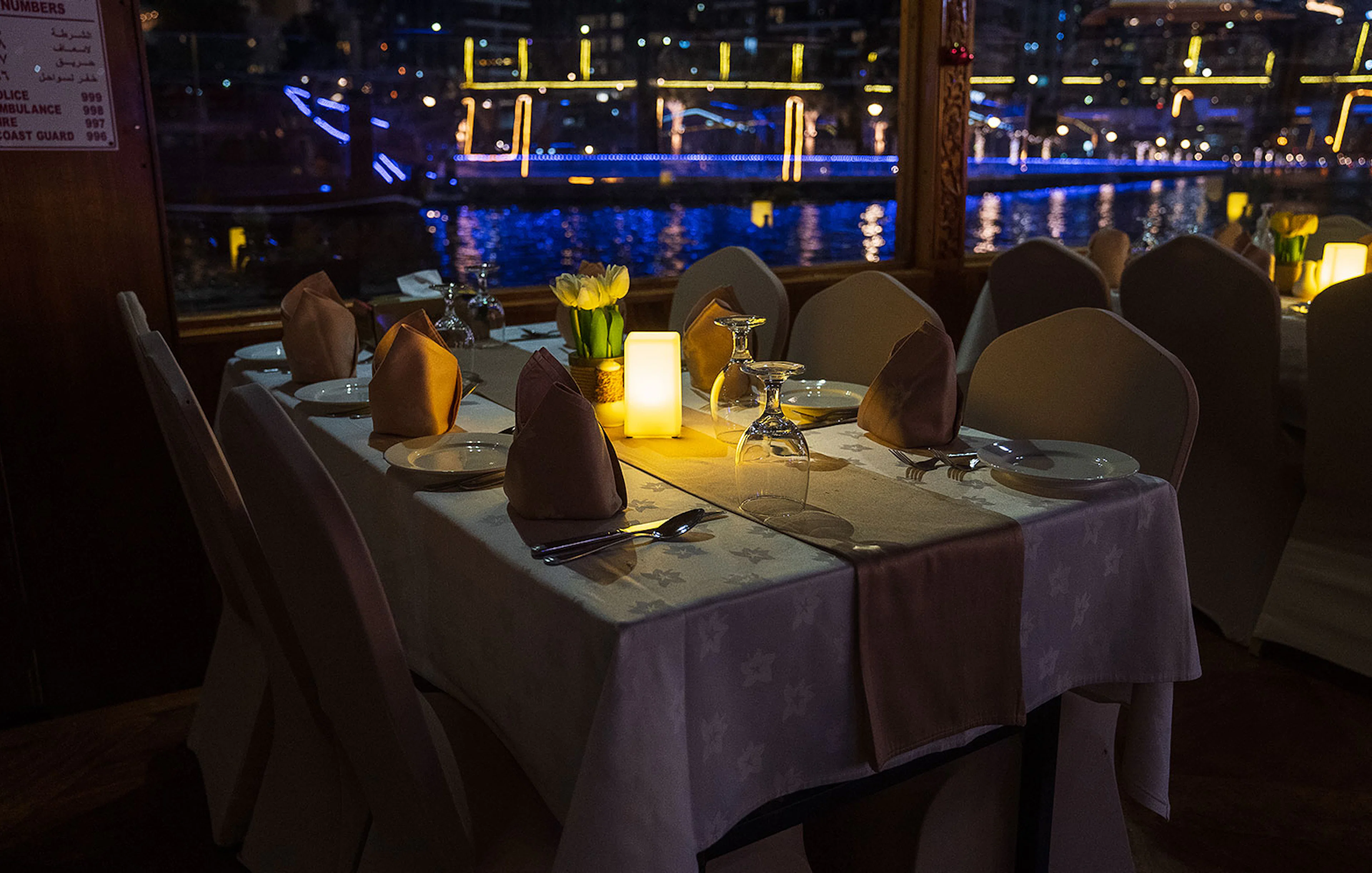 Dining table setup on a Dhow Cruise with views of Dubai Creek at night.