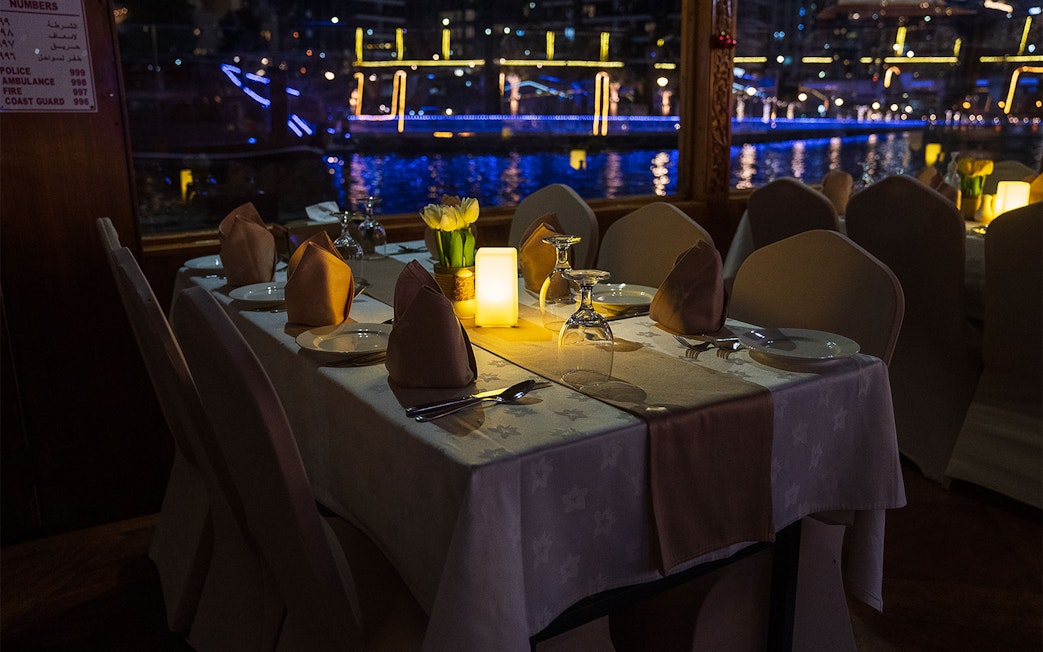 Dining table setup on a Dhow Cruise with views of Dubai Creek at night.