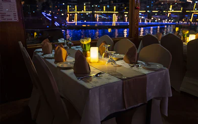 Dining table setup on a Dhow Cruise with views of Dubai Creek at night.