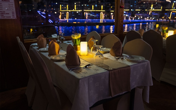 Dining table setup on a Dhow Cruise with views of Dubai Creek at night.