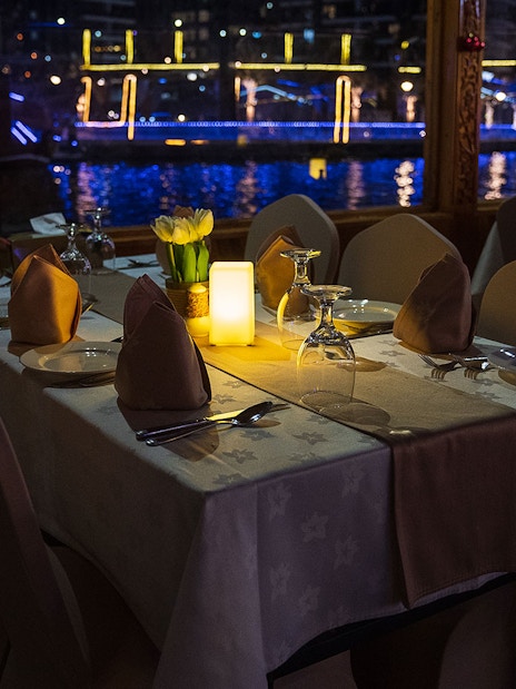 Dining table setup on a Dhow Cruise with views of Dubai Creek at night.