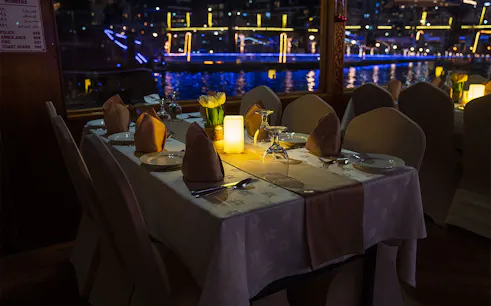 Dining table setup on a Dhow Cruise with views of Dubai Creek at night.
