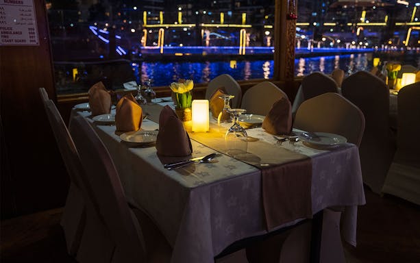 Dining table setup on a Dhow Cruise with views of Dubai Creek at night.