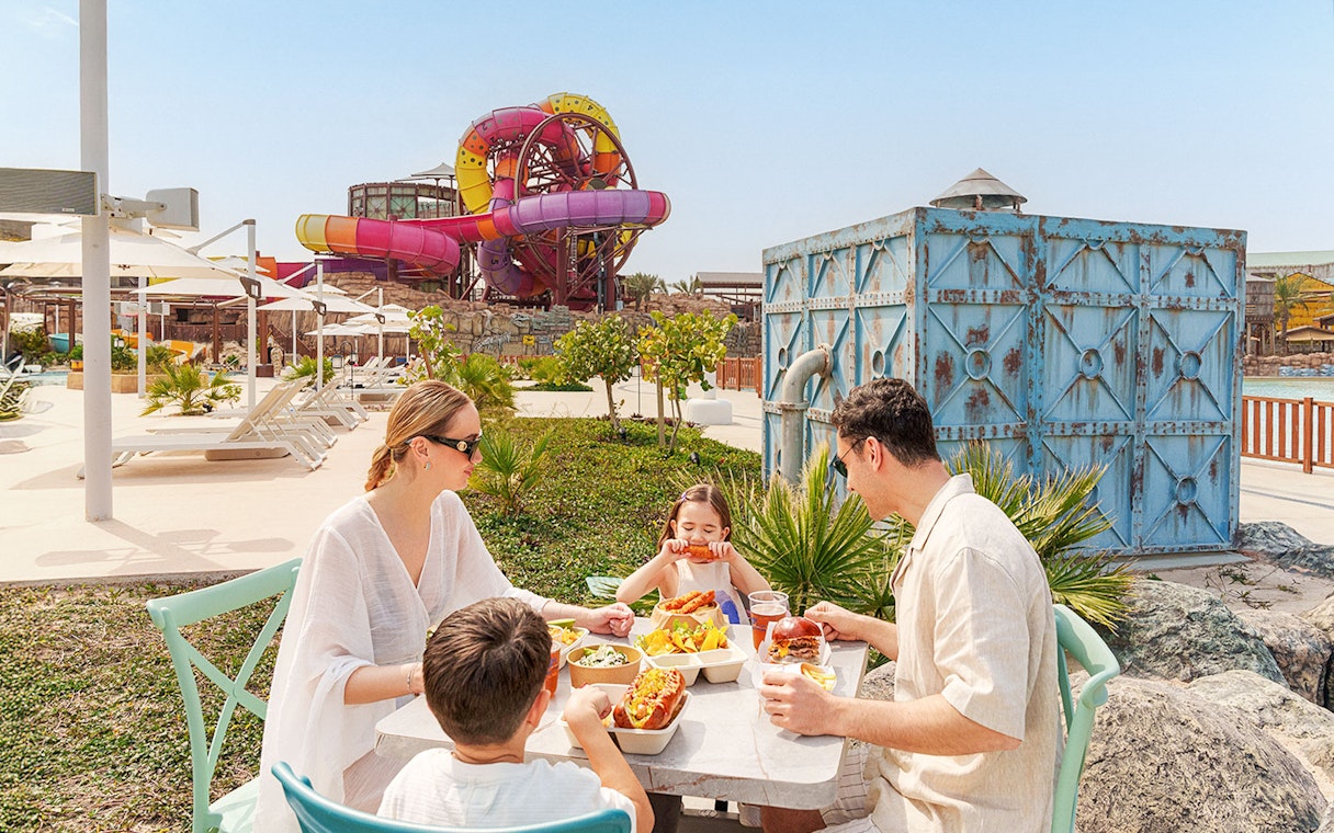 Visitors enjoying a meal at Meryal Waterpark with colorful slides in the background.