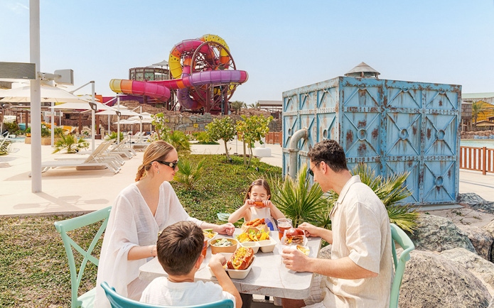 Visitors enjoying a meal at Meryal Waterpark with colorful slides in the background.