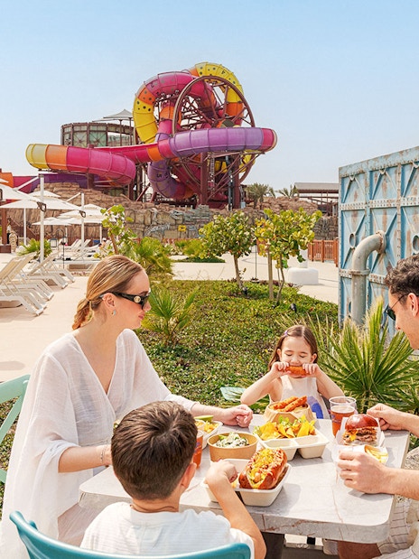 Visitors enjoying a meal at Meryal Waterpark with colorful slides in the background.
