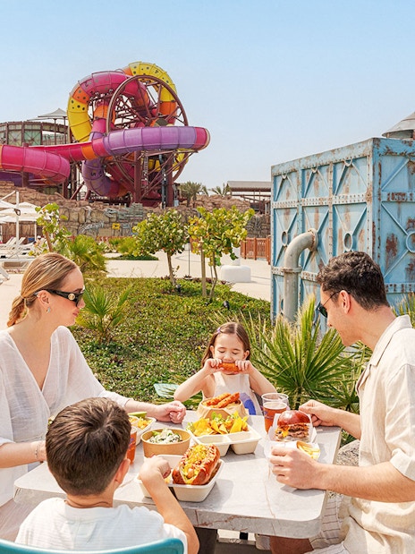 Visitors enjoying a meal at Meryal Waterpark with colorful slides in the background.
