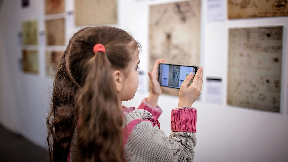 Girl using Rijksmuseum app to explore art exhibit.