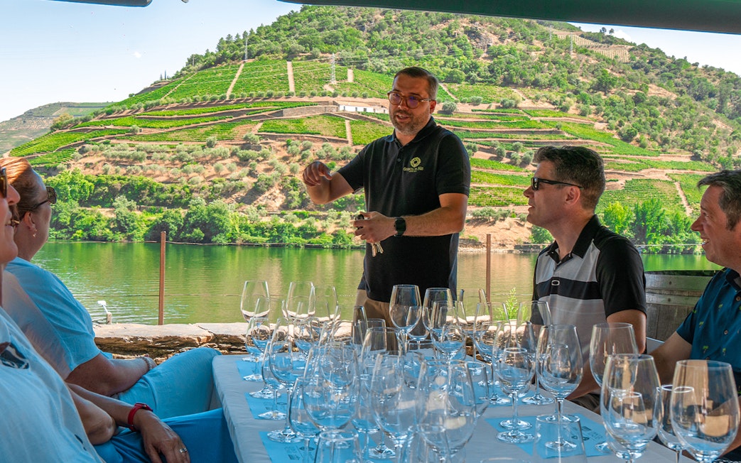 Tourists tasting wine with a guide overlooking the Douro Valley vineyards.