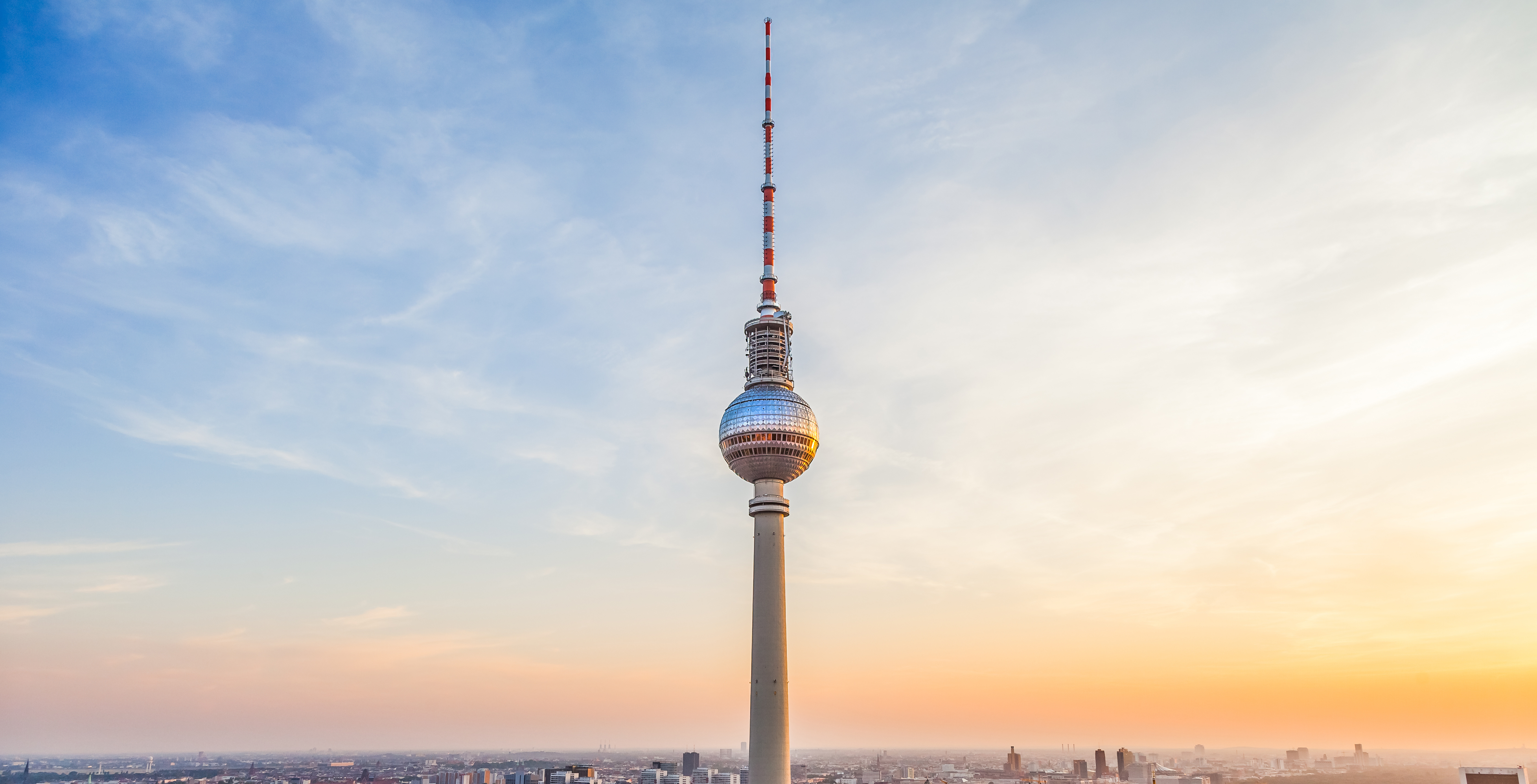 Berlin TV Tower at sunset with cityscape below.