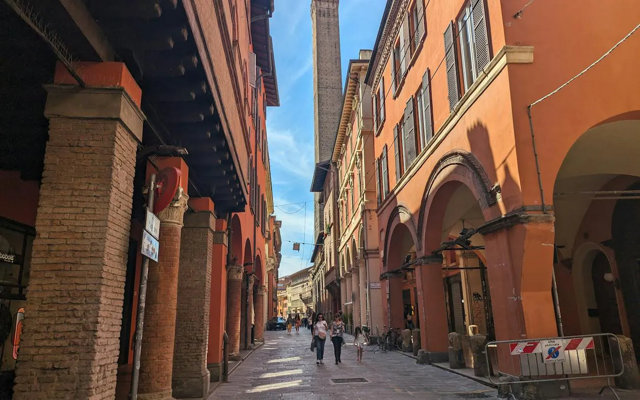 Bologna street with historic porticoes and tower, part of self-guided city exploration game.